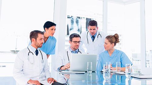 Médicos en torno a una mesa con una computadora y una placa detrás