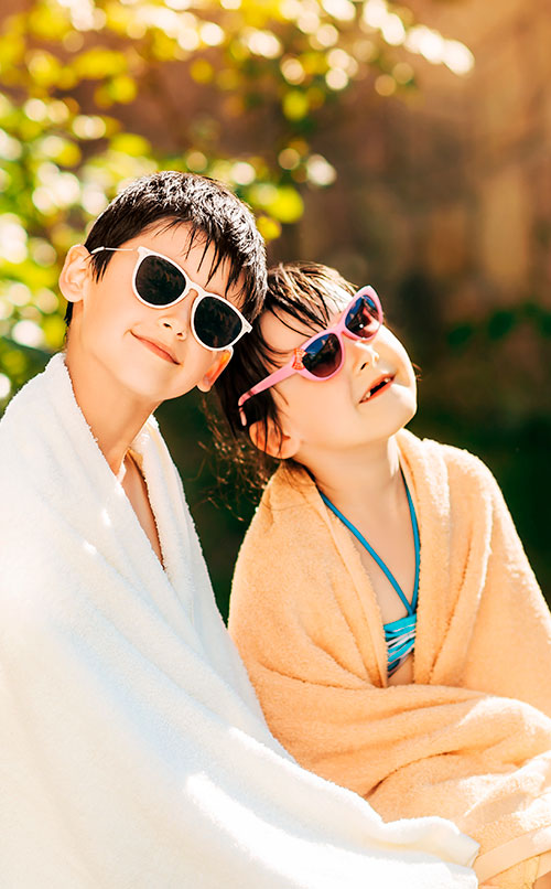 un niño y una niña envueltos en una toalla, sentados al sol con lentes de sol