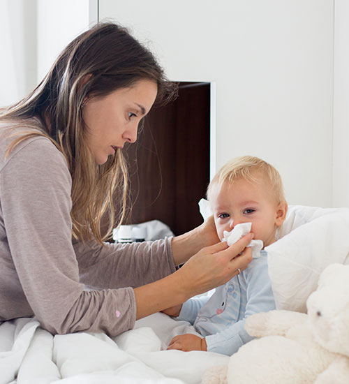 Madre limpiando la nariz a un bebe - Vacunas, consideraciones a tener presentes