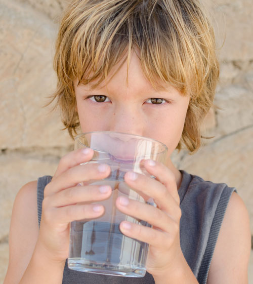 Niño bebiendo un vaso de agua | ¿Cómo evitamos la deshidratación en niños durante el verano?