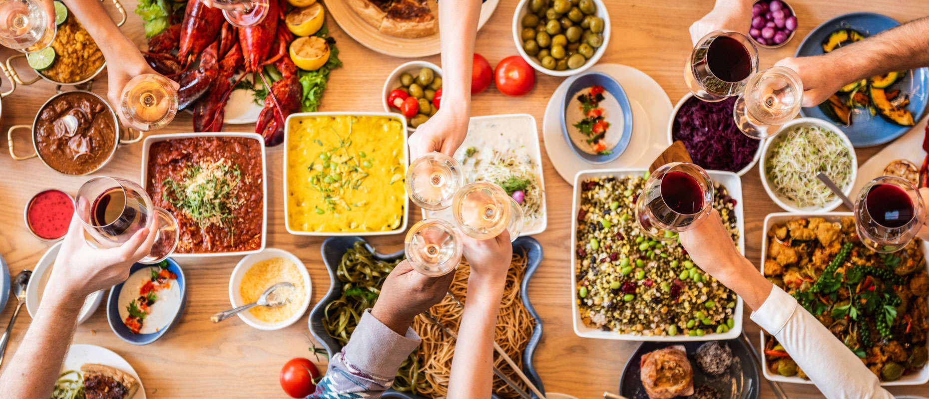 Mesa vista de arriba con diferentes tipos de comida y varios brazos con copas brindando | Acidez estomacal Mesa vista de arriba con diferentes tipos de comida y varios brazos con copas brindando | Acidez estomacal