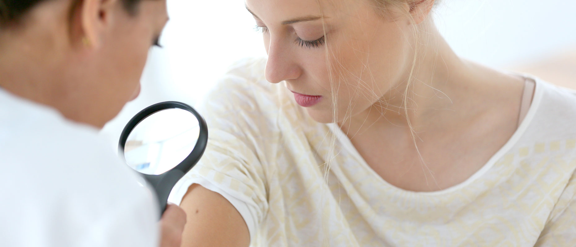 Doctora mirando el brazo de una paciente con una lupa | Cáncer de piel: la importancia de detectarlo a tiempo Doctora mirando el brazo de una paciente con una lupa | Cáncer de piel: la importancia de detectarlo a tiempo