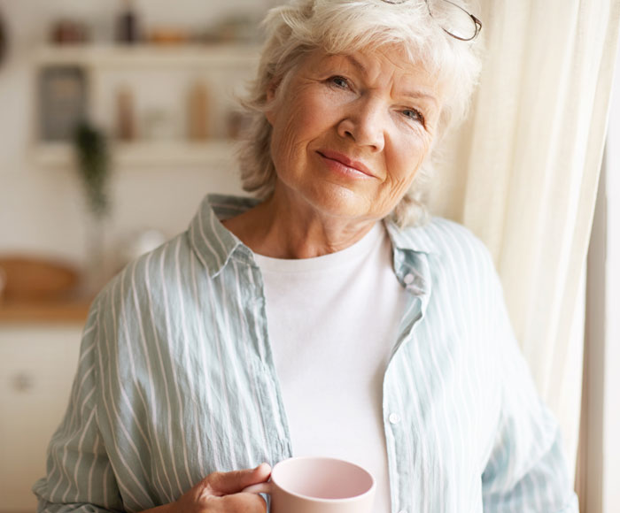 Adulta mayor sonriendo, con una taza de café en su mano | Beneficios MP