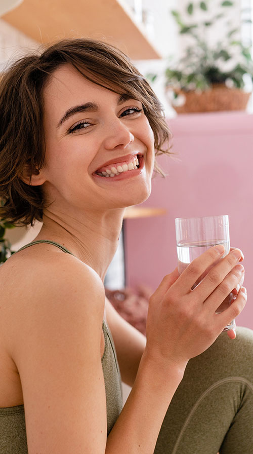 Mujer sonriendo con un vaso de agua en la mano | Endometriosis: entender sus señales para un diagnóstico temprano