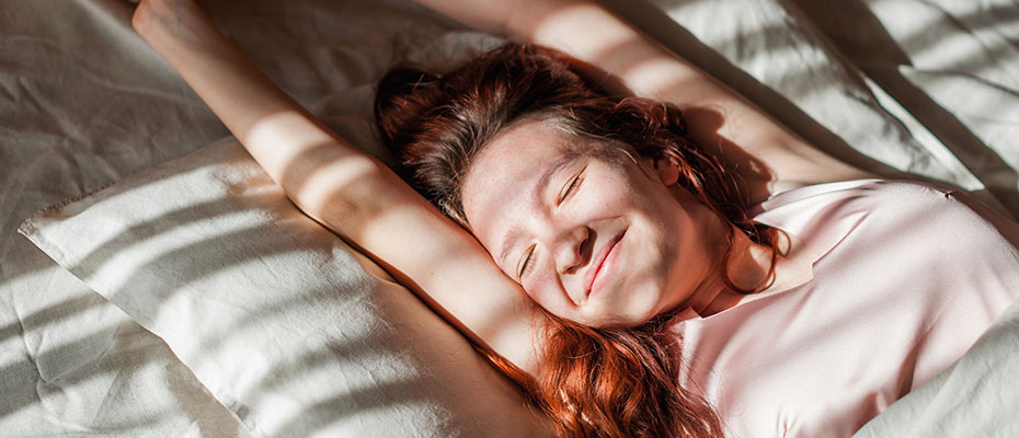 Mujer desperezándose sonriente en la cama | Sueño saludable: claves para un mejor descanso