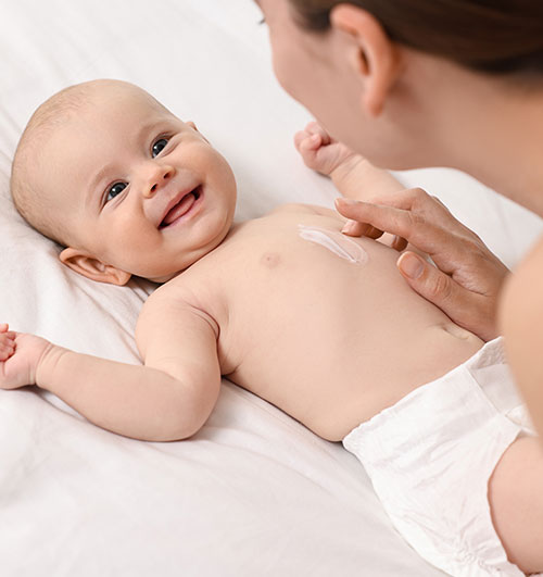 Madre colocándole crema en el cuerpo a un bebé | Vivir con dermatitis atópica: cómo entenderla mejor