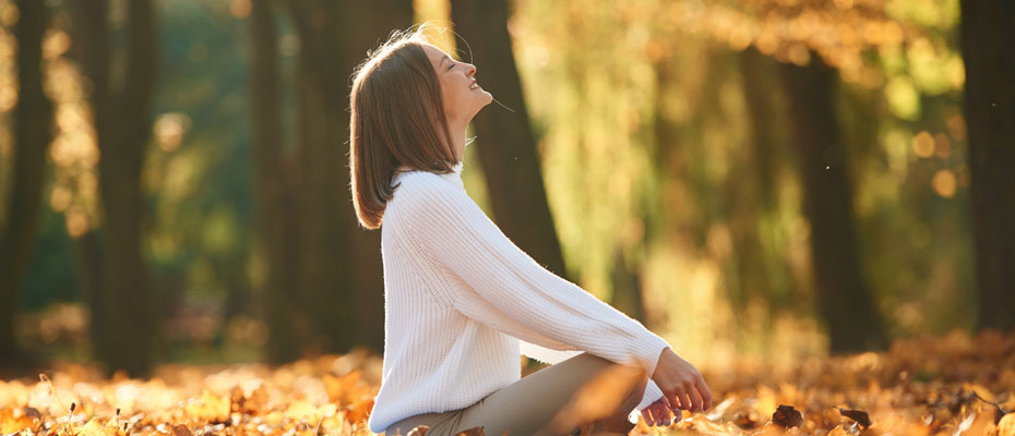 Mujer tomando aire al sol sentada sobre hojas de otoño | Asma: entenderla para respirar mejor