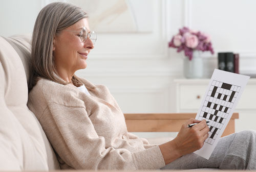 Mujer adulta en el sillón de si cada haciendo crucigramas | Longevidad saludable