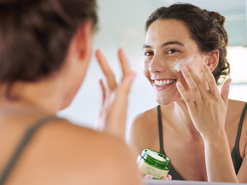 Mujer poniéndose crema en la cara frente a un espejo | Rutina de skincare: ni todo el mundo, ni todo el tiempo