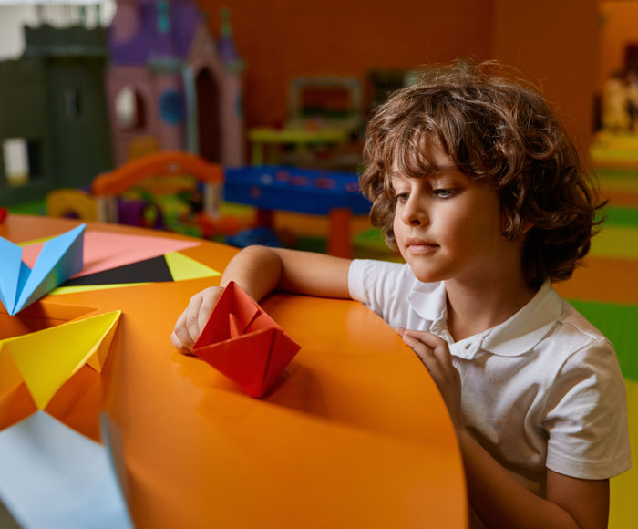 Niño jugando con un barco de papel en una clase de escuela | Beneficios MP